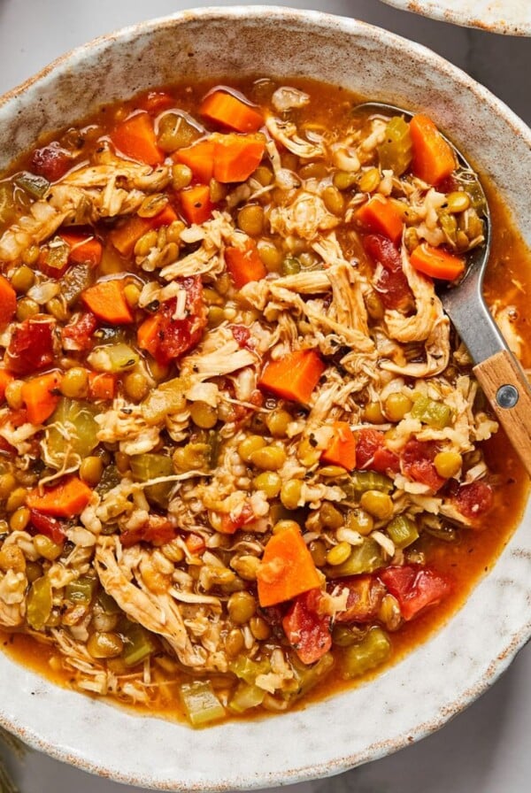 A bowl of chicken lentil soup in a bowl with a spoon resting in the side of the bowl.