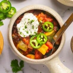 A bowl of black bean chili on the table with sour cream and jalapeno slices on top.