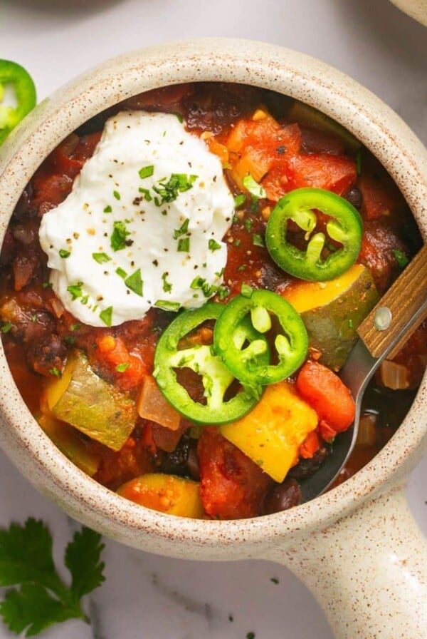 A bowl of black bean chili on the table with sour cream and jalapeno slices on top.