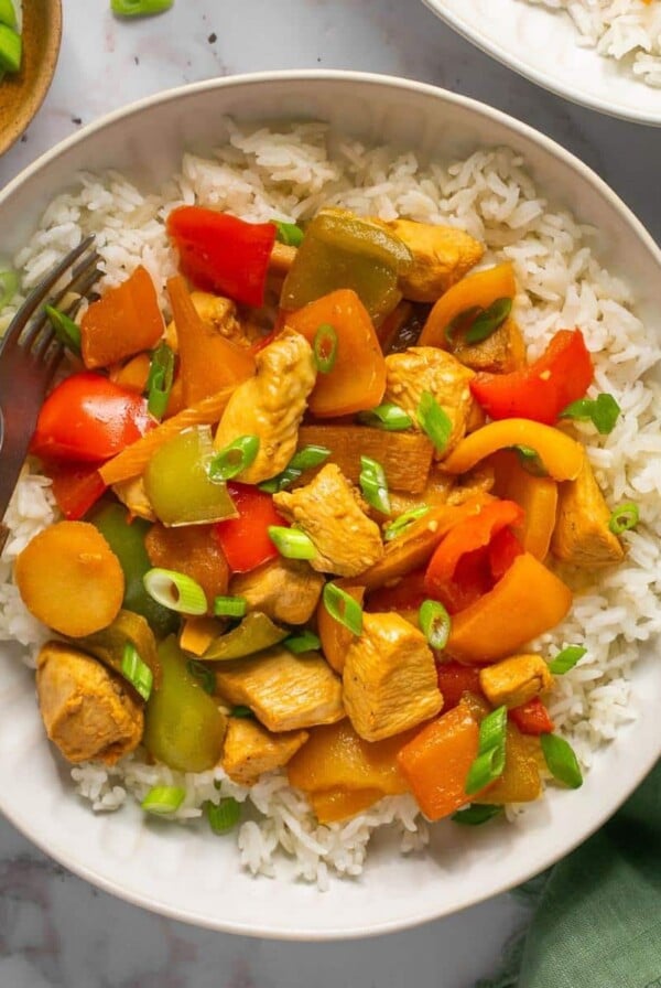 A healthy chicken stir fry in a bowl with a fork and bowl of green onion.