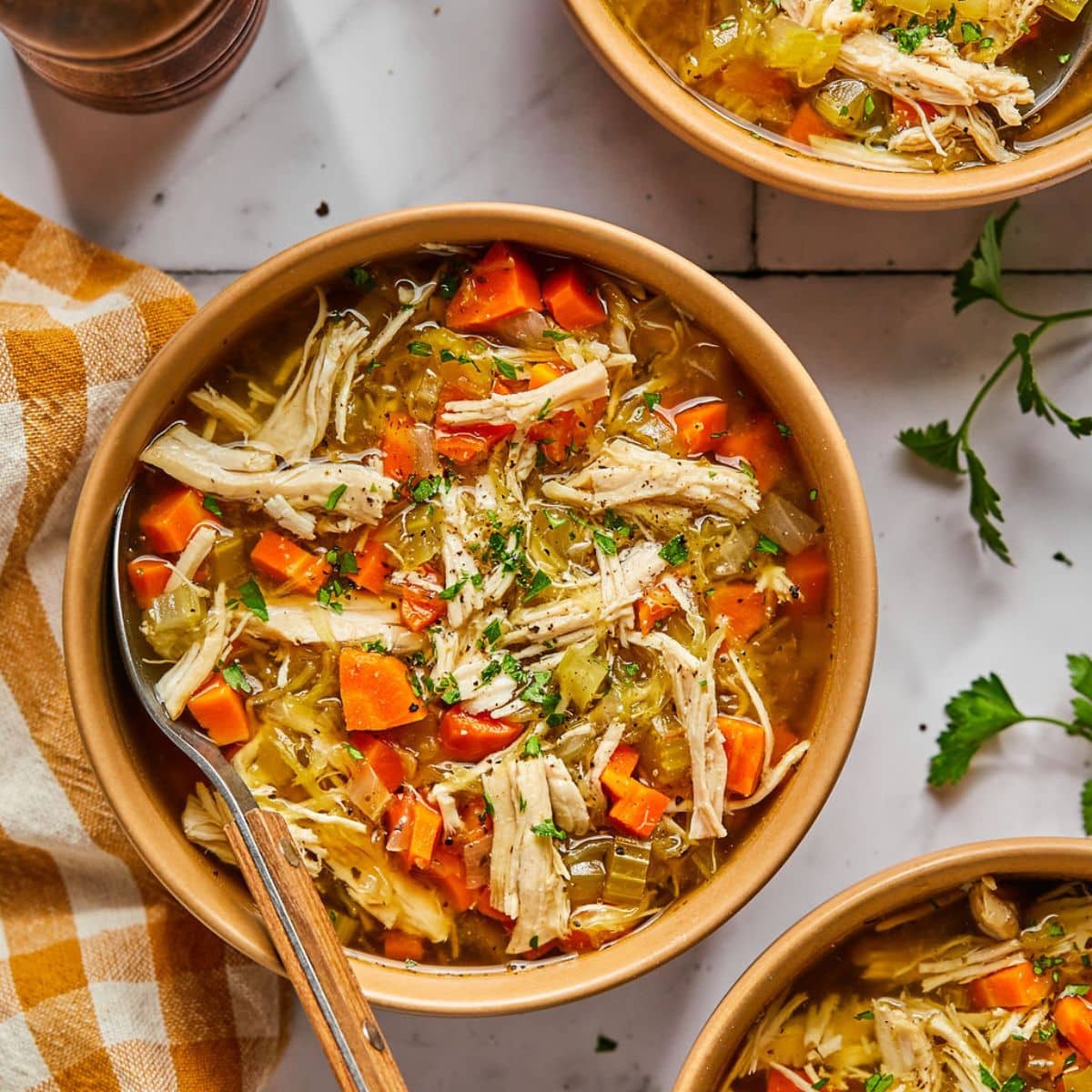 chicken soup in a brown wooden bowl with a spoon in it.