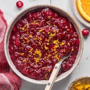 A bowl of sugar free cranberry sauce on the table with orange zest on top and a spoon in the bowl.