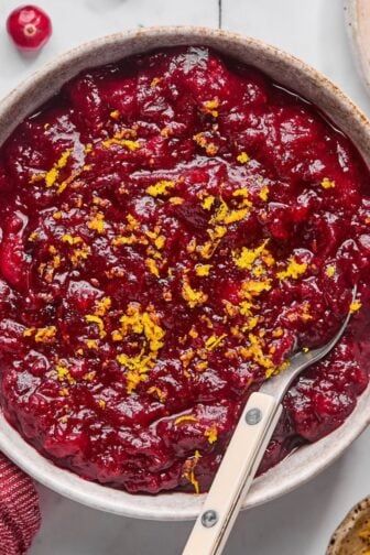 A bowl of sugar free cranberry sauce on the table with orange zest on top and a spoon in the bowl.