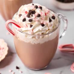 Mug of peppermint mochas on a table with a small dish of crushed peppermint candy.