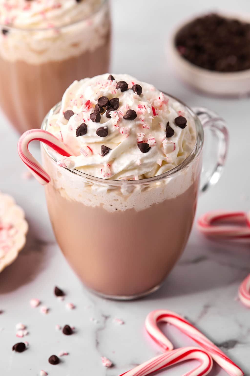 A clear mug of skinny peppermint mocha latte topped with whipped cream, chocolate chips, and peppermint candy.