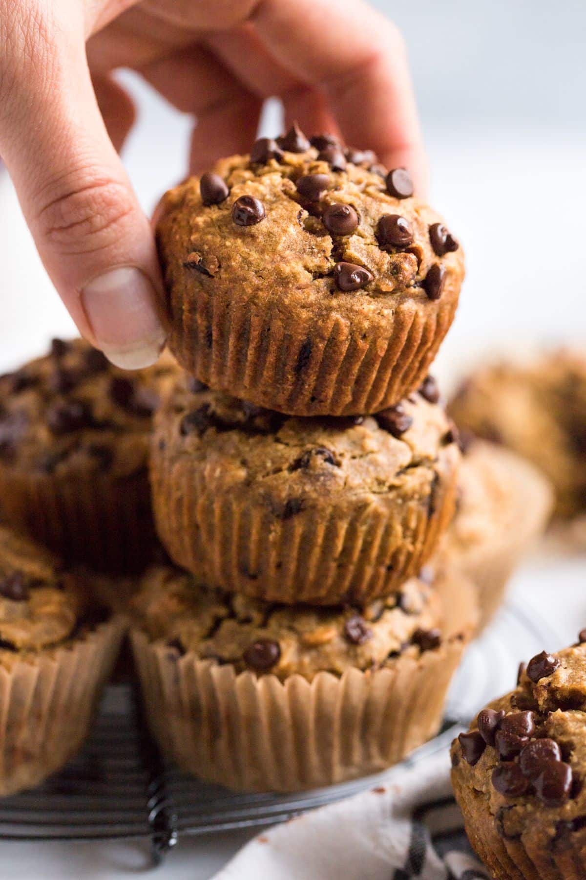 A stack of butternut squash muffins with chocolate chips on top and a hand reaching to grab one.