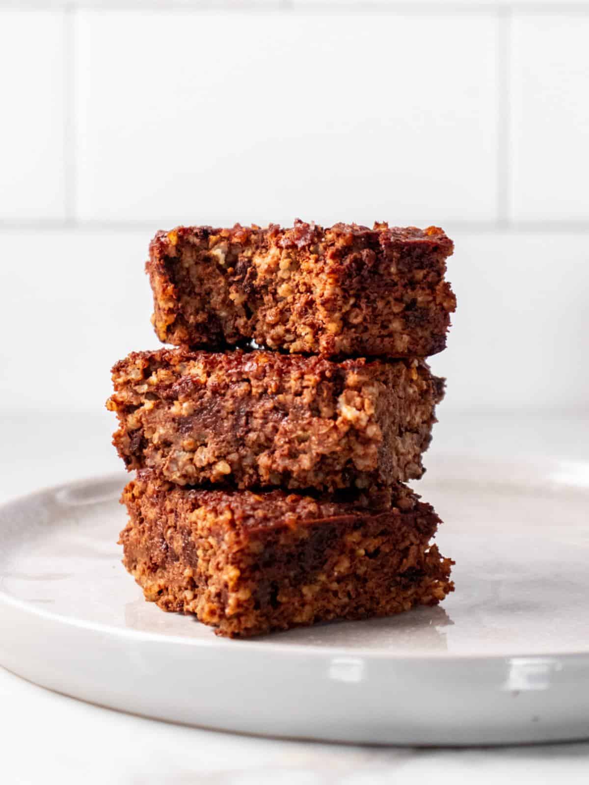 Three quinoa brownies stacked on top of each other on a white plate.
