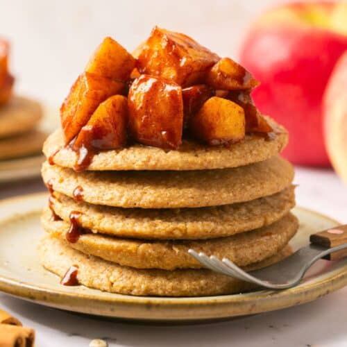 A stack of apple pancakes on a plate with a fork to the side.