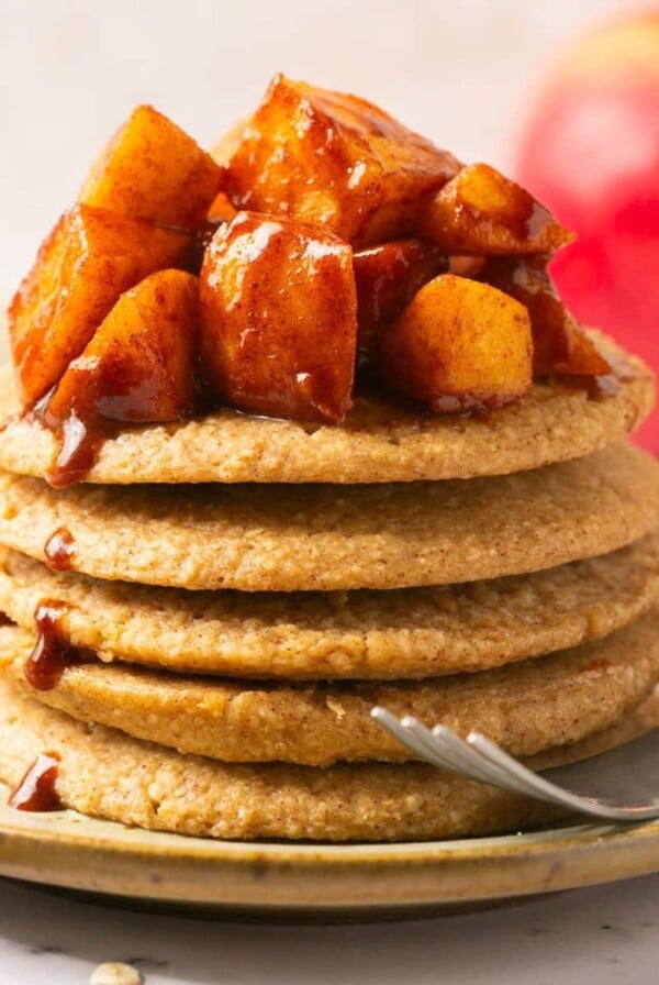 A stack of apple pancakes on a plate with a fork to the side.
