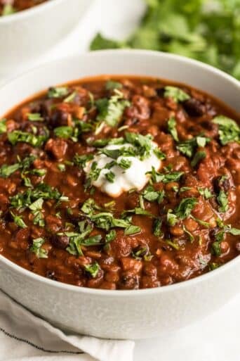 A bowl of lentil and black bean chili on the table with a spoon of greek yogurt on top.