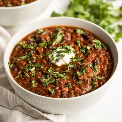 A bowl of lentil and black bean chili on the table with a spoon of greek yogurt on top.