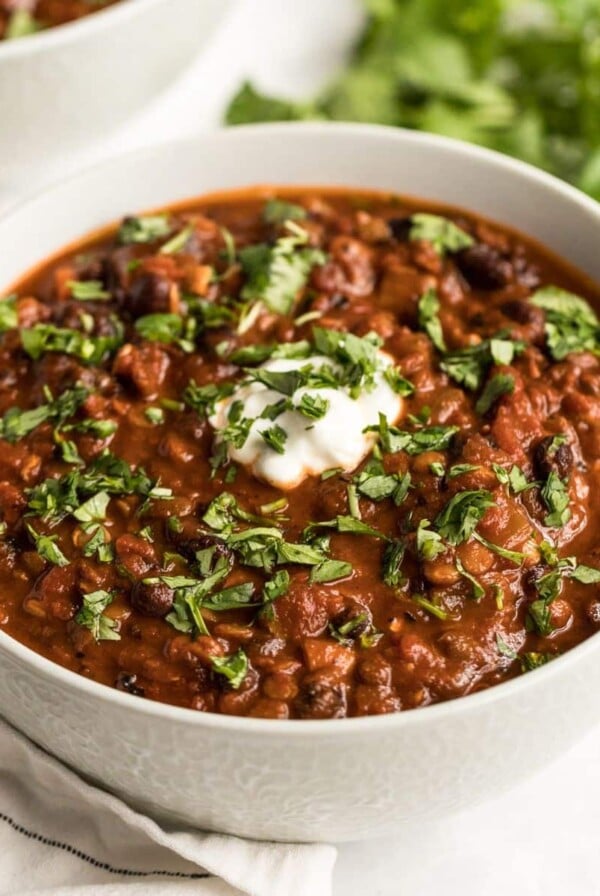 A bowl of lentil and black bean chili on the table with a spoon of greek yogurt on top.