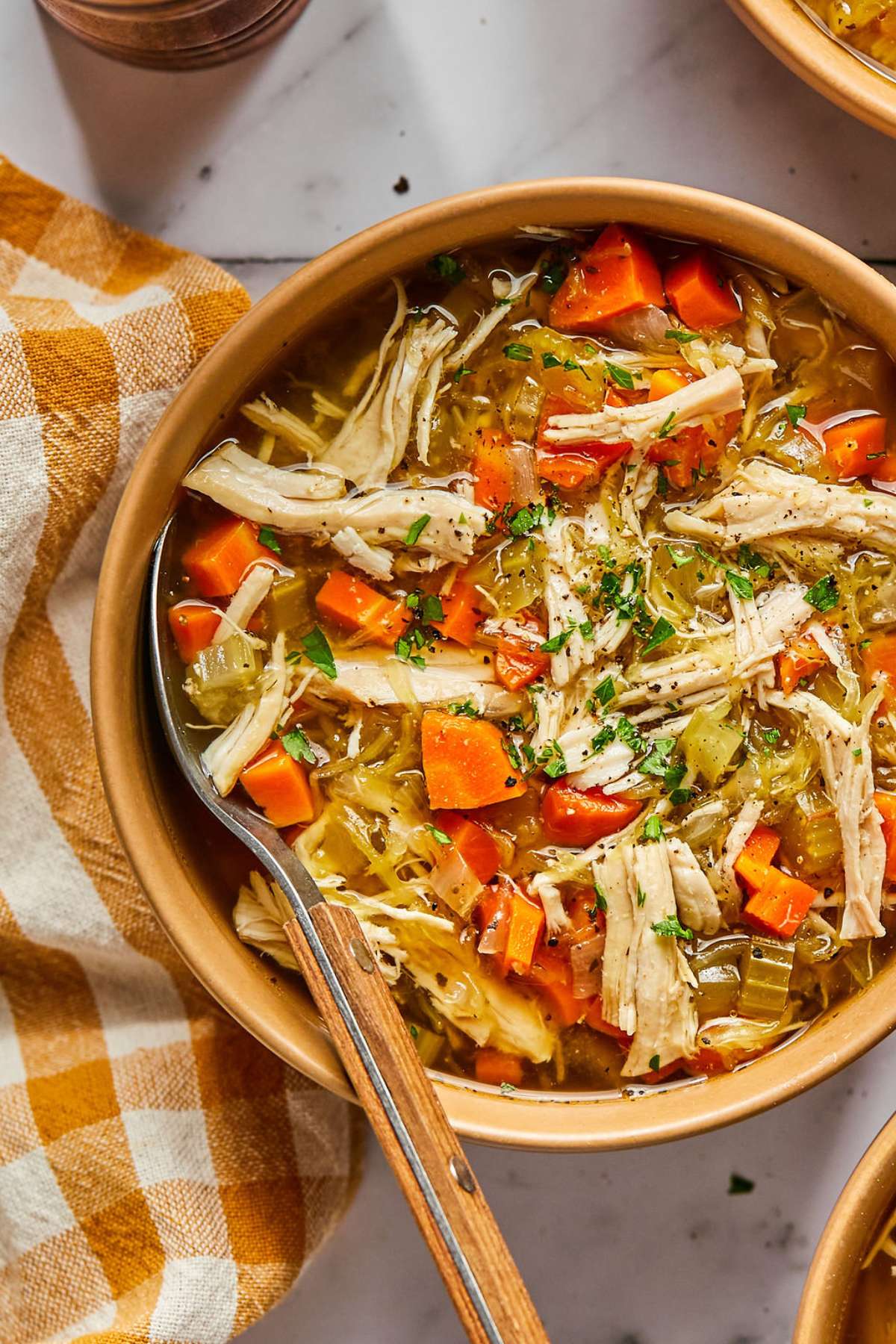 A bowl of chicken soup without noodles on the table with a spoon resting on the edge of the bowl. 