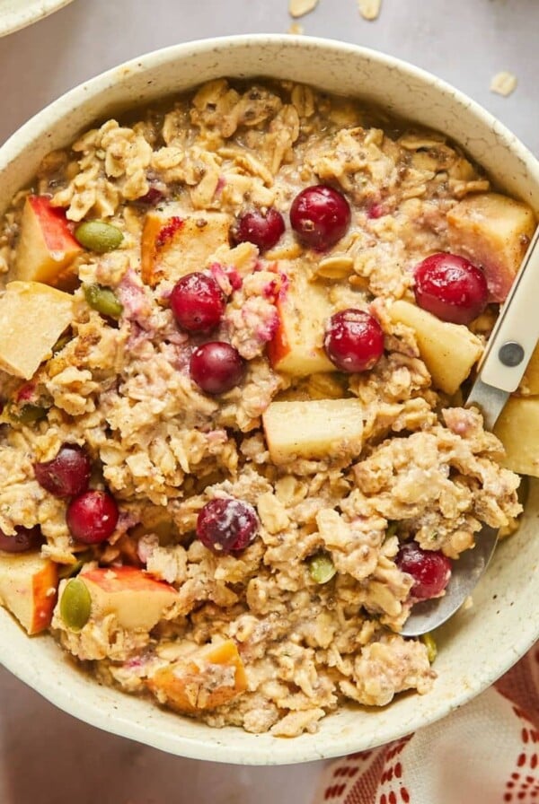 A bowl of cranberry apple crockpot oatmeal on the table with a spoon resting in the bowl.