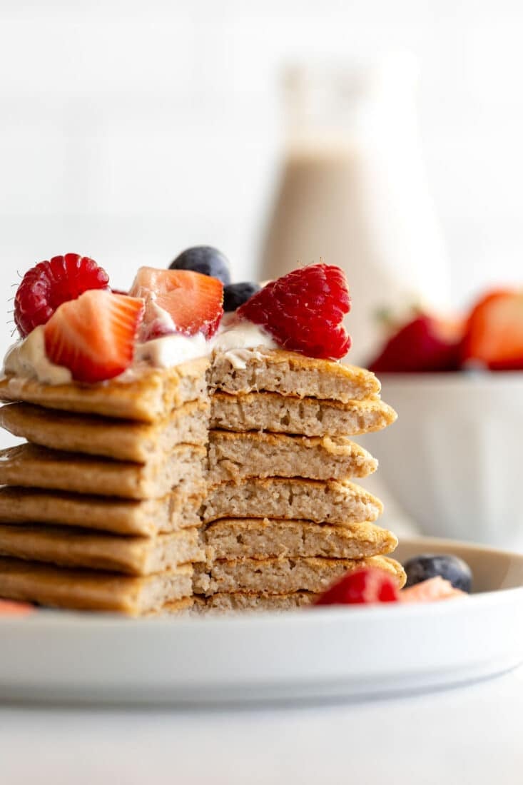 Oatmeal cottage cheese pancakes stacked up on a plate and topped with yogurt and berries and it's missing a portion so you can see the inside of the pancakes.