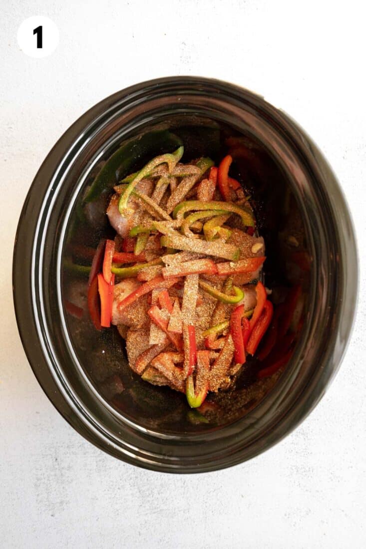 Chicken and peppers topped with seasoning in a slow cooker.
