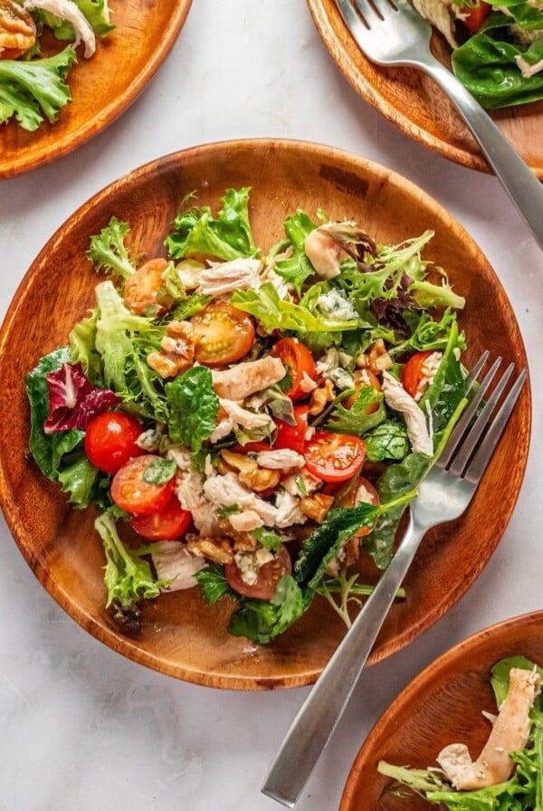 Gorgonzola salad with chicken and tomatoes on wooden plate with forks resting on the side.