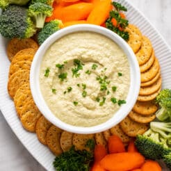 hummus in a white bowl with a platter of crackers