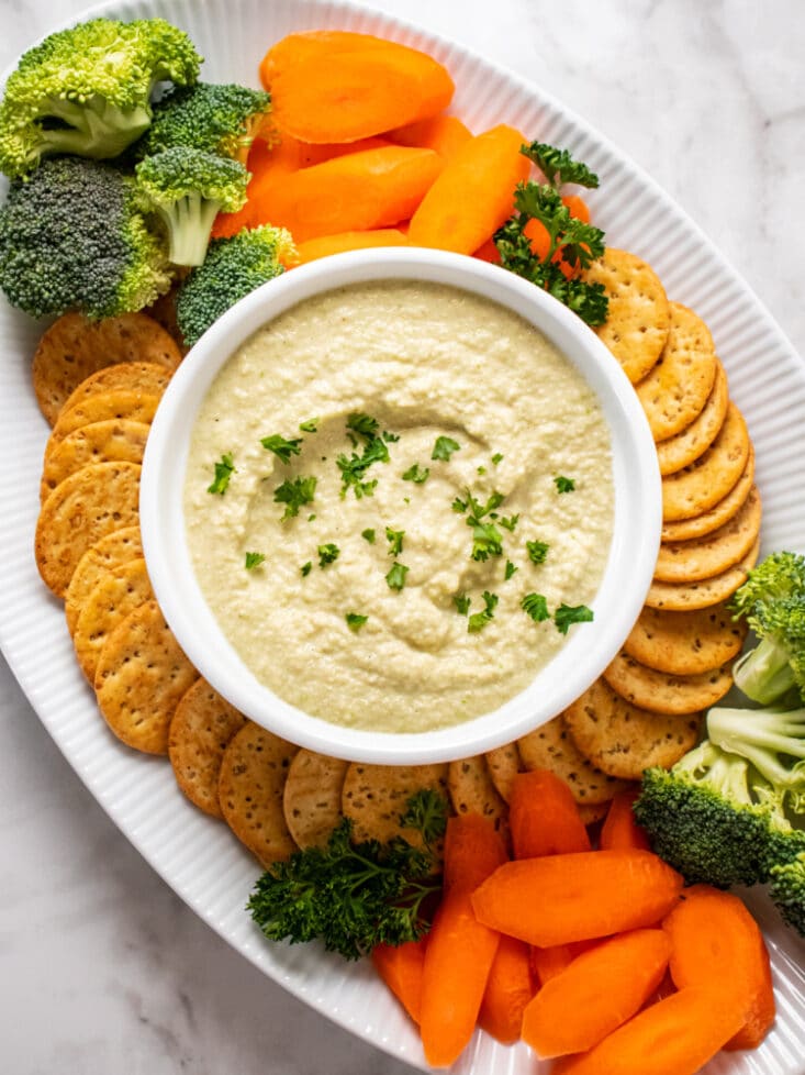 hummus in a white bowl with a platter of crackers