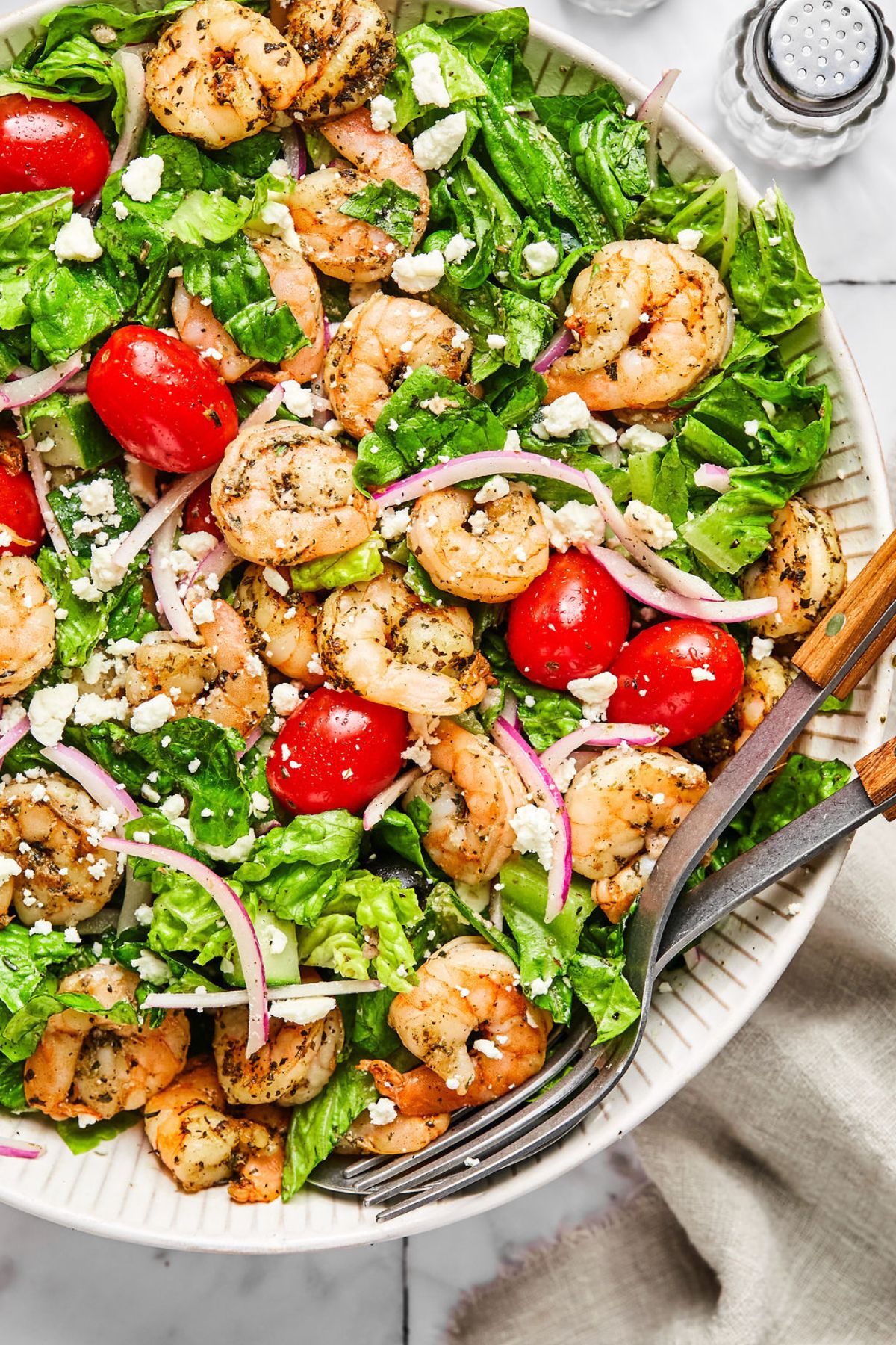 Greek salad with shrimp in a white bowl with a knife and form on the side.