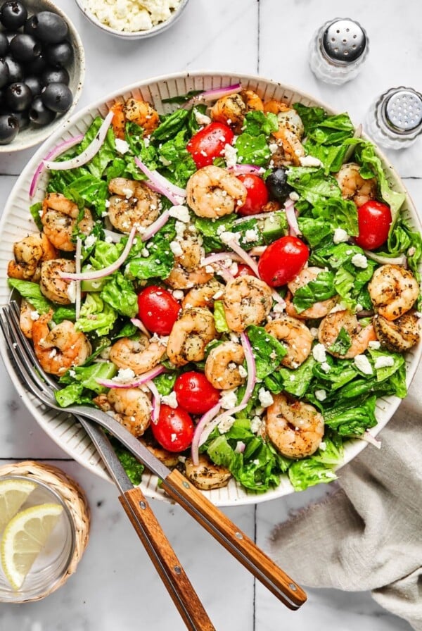 greek salad with shrimp in a white bowl with knife and fork