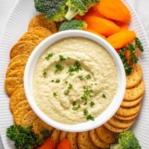 A bowl of zucchini hummus with veggies and crackers on the side.