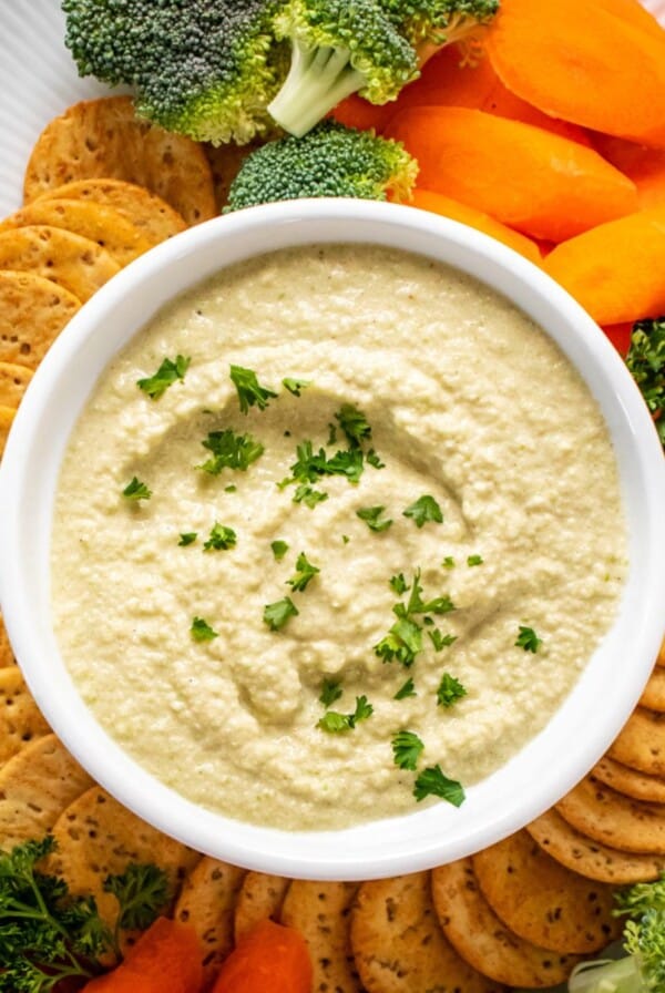 A bowl of zucchini hummus with veggies and crackers on the side.