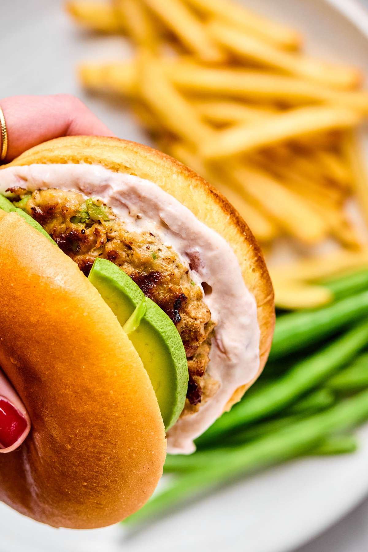 A hand holding a grilled ground chicken burger up over a plate.
