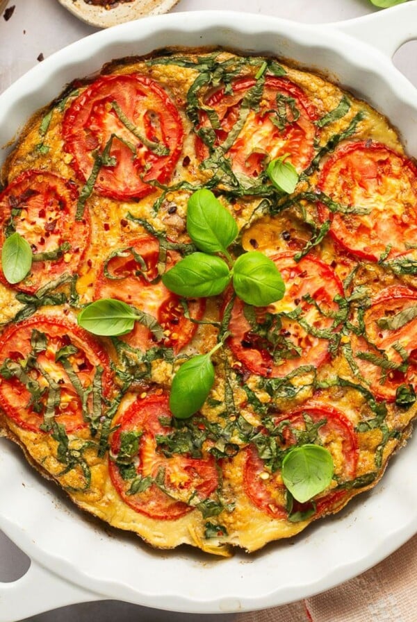 A tomato egg and sausage casserole in a white round baking dish on a table top.