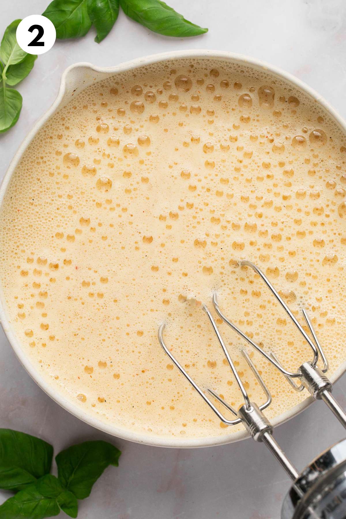 Bubbly egg mixture with whisk paddles leaning on the edge of the bowl.