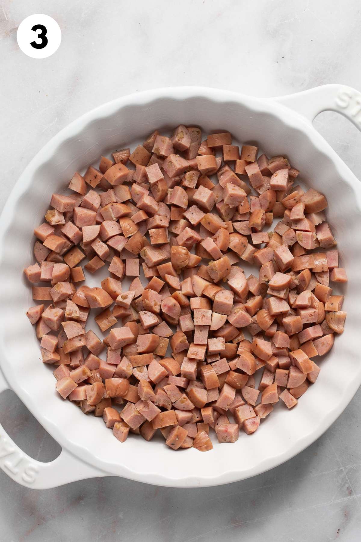 Sausage sprinkled in the bottom of a round baking dish.