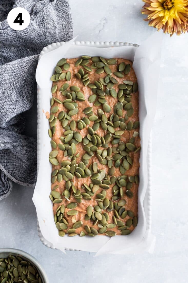 Paleo pumpkin bread batter poured into a lined loaf pan and topped with pumpkin seeds.