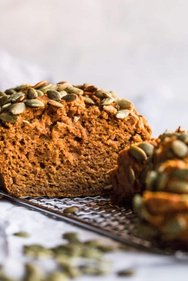 Gluten free sugar free pumpkin bread on a wire rack with a few slices cut and leaning over in front.
