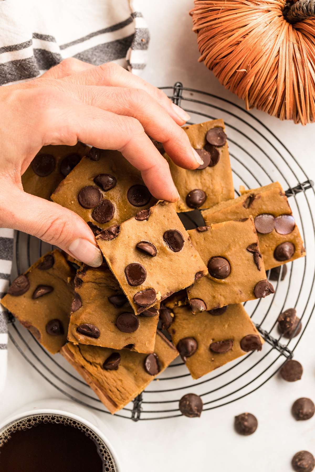 A hand reaching to grab a pumpkin protein bar with chocolate chips stacked up on a rack.