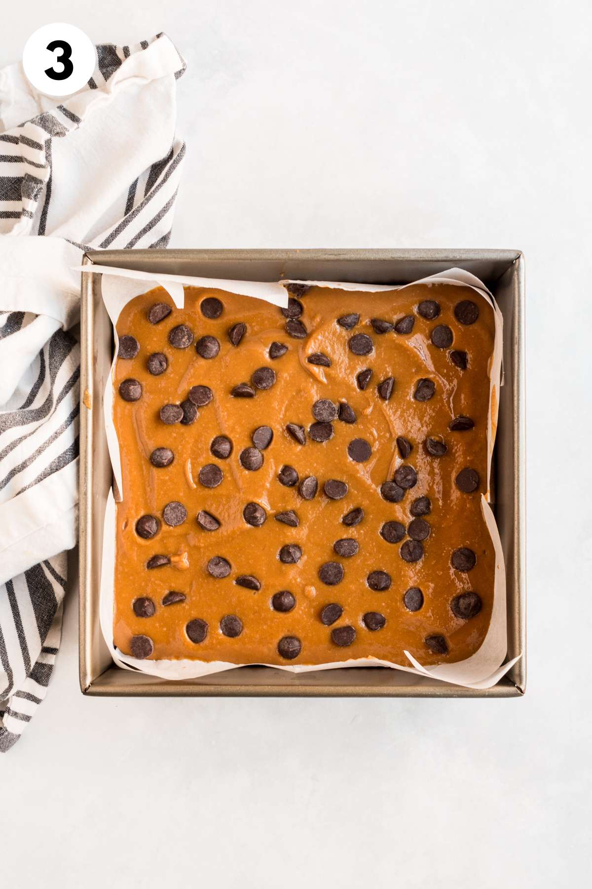 Pumpkin protein bar mixture in a baking pan topped with chocolate chips.