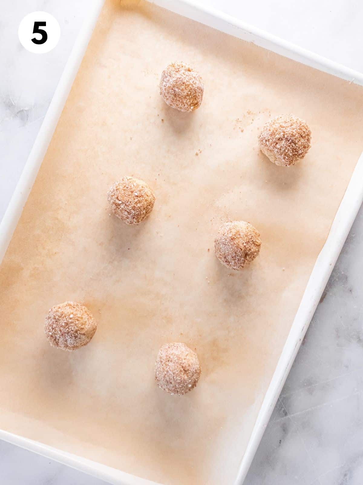 Cookie dough balls laid out on a parchment lined baking tray.
