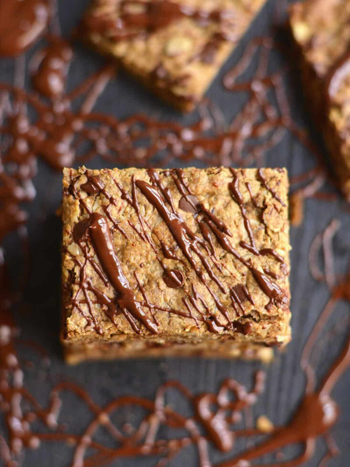 A single chocolate chip peanut butter granola bar drizzled with chocolate on a plate.
