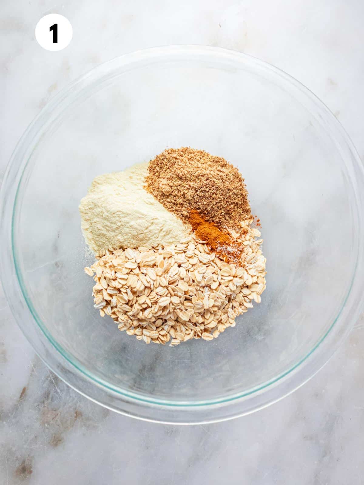 Oatmeal and other dry ingredients added to a glass bowl.
