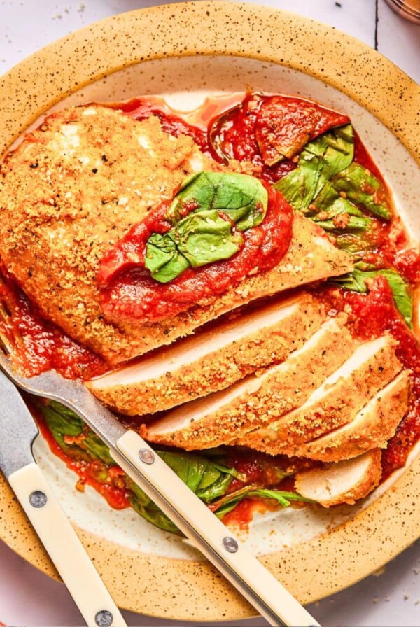 A plate of sheet pan chicken parmesan on a plate with some sliced.
