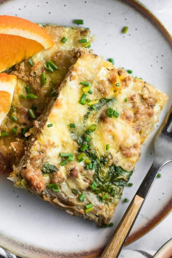 A square of sheet pan sausage breakfast pizza on a plate with orange slices.