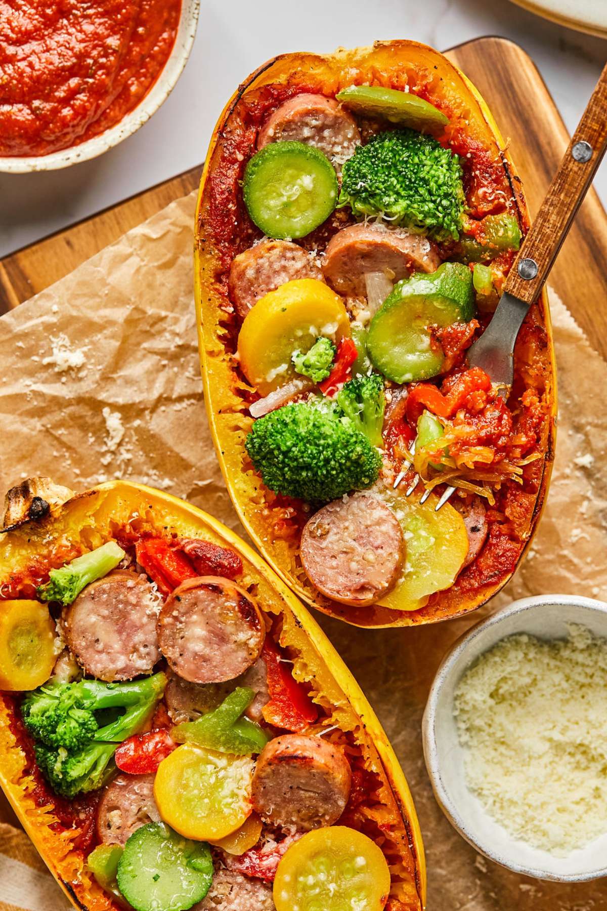 Two spaghetti squash pizza boats on a piece of parchment with a fork resting on one with a bite on it. 