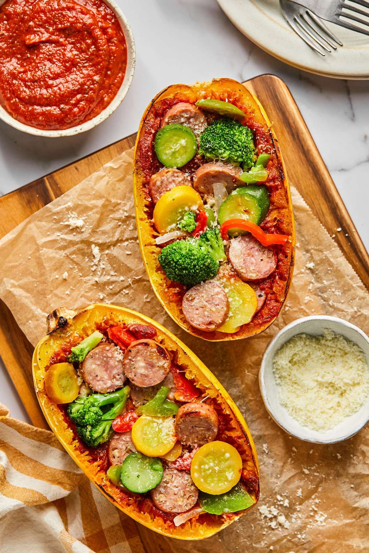 Two spaghetti squash pizza boats on a baking tray with a bowl of parmesan to the side.