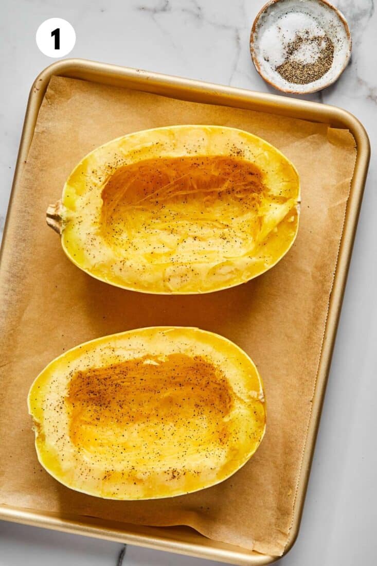 Spaghetti squash cut in half and seeds scooped out on a baking tray.