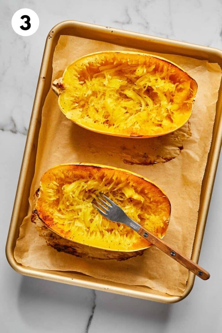 Spaghetti squash on a baking tray with a fork in one after scraping the noodle free.