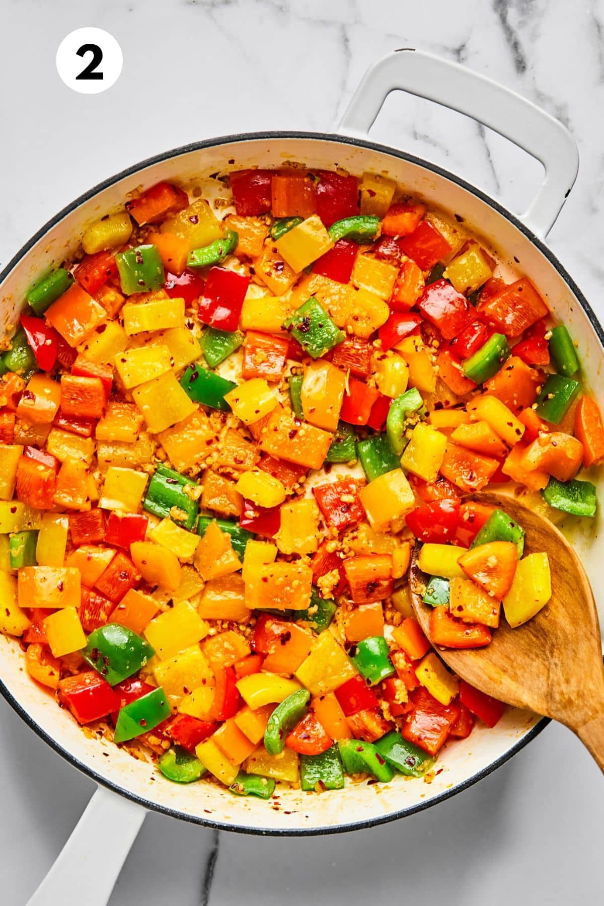Vegetables cooking in a skillet with a wooden spoon lifting some up.
