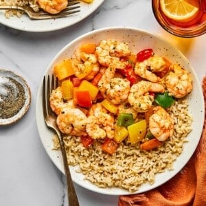 A colorful shrimp and rice recipe on a white plate with bell peppers.