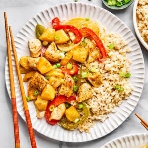 Healthy sweet and sour chicken served on a white plate with chopsticks resting on the edge of the plate.