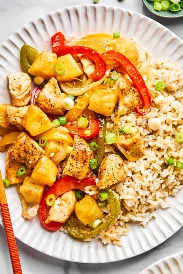 Healthy sweet and sour chicken served on a white plate with chopsticks resting on the edge of the plate.