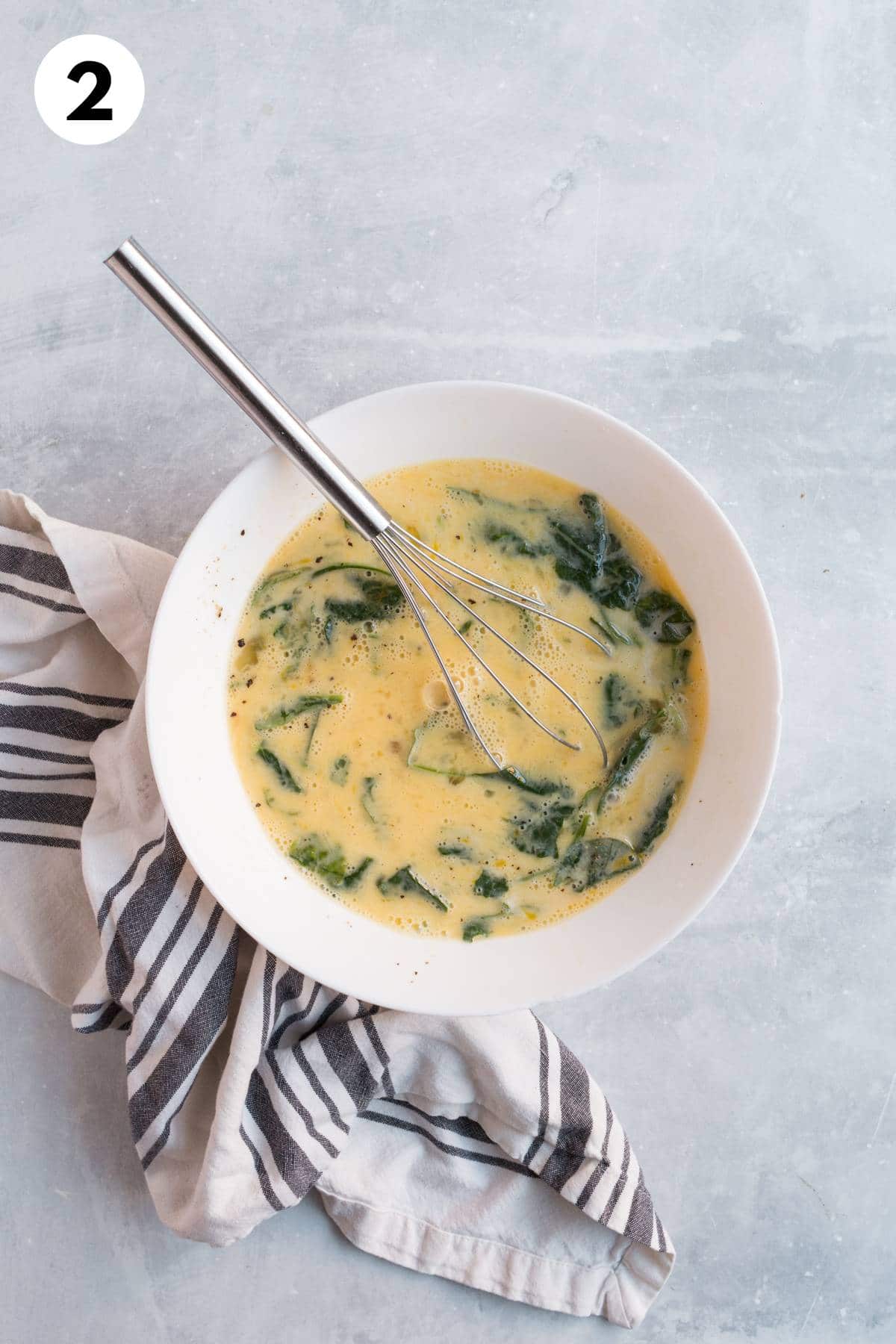 Eggs and spinach mixed in a bowl with a whisk.