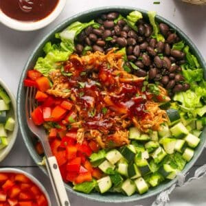 A BBQ chicken bowl on the table with a fork in the bowl and it's topped with chicken, black beans, bell pepper, and zucchini.
